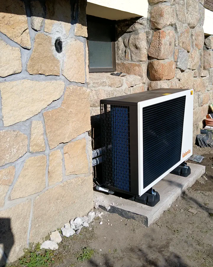 Instaladores de calefacción en Becerril de la Sierra 4 Unidad exterior de aerotermia Lasian junto a una fachada de piedra de un chalet. Instalación de Guzmán Calefacción
