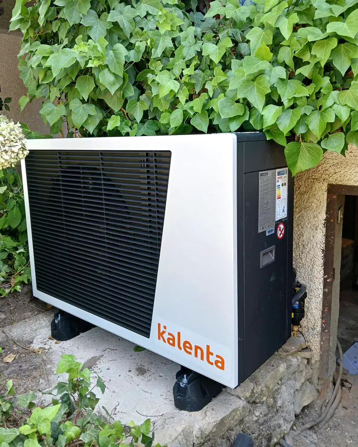 Unidad exterior de aerotermia Kalenta instalada bajo una enredadera en una casa de piedra. Instalación de Guzmán Calefacción