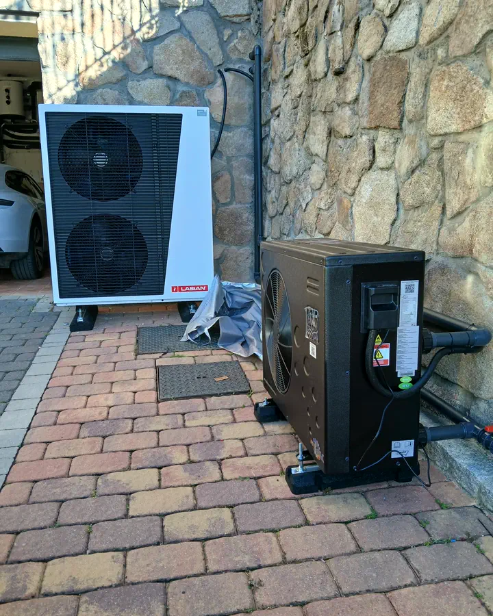 Instaladores de calefacción en Collado Mediano 4 Dos unidades exteriores de aerotermia en el patio adoquinado de una vivienda con fachada de piedra. Instalación de Guzmán Calefacción