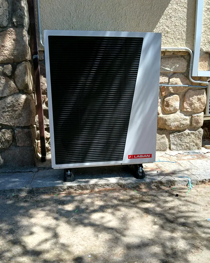 Instaladores de calefacción en Hoyo de Manzanares 4 Unidad exterior de aerotermia Lasian junto a un muro de granito, a la sombra de los árboles. Instalación de Guzmán Calefacción