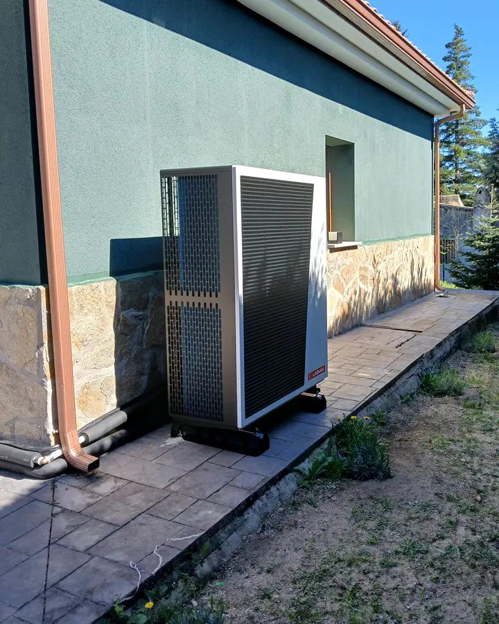 Unidad exterior de aerotermia junto a la fachada lateral de un chalet con jardín. Instalación de Guzmán Calefacción