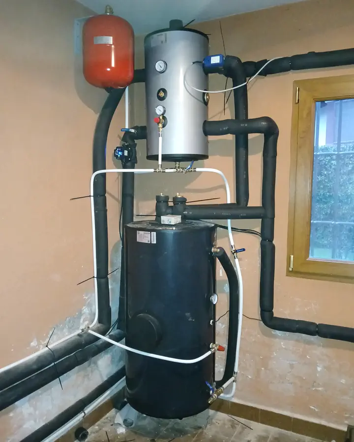 Depósito de inercia y acumulador de agua caliente con vaso de expansión en una sala técnica con ventana. Instalación de Guzmán Calefacción