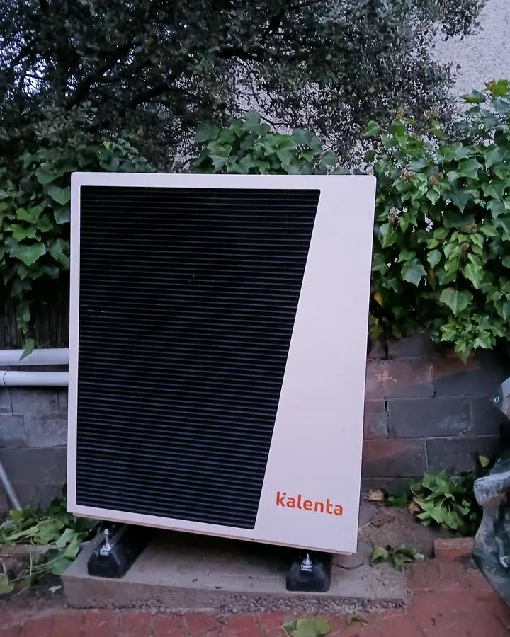 Unidad exterior de aerotermia Kalenta junto a un seto y vegetación en el jardín de un chalet. Instalación de Guzmán Calefacción