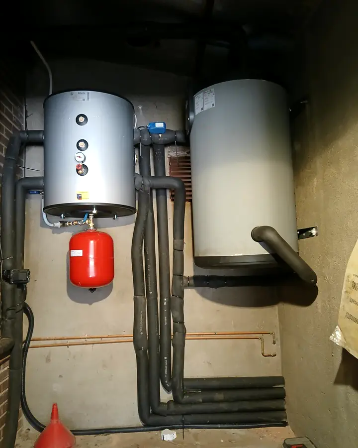 Dos acumuladores de agua caliente con vaso de expansión y tuberías aisladas en un cuarto de calderas. Instalación de Guzmán Calefacción