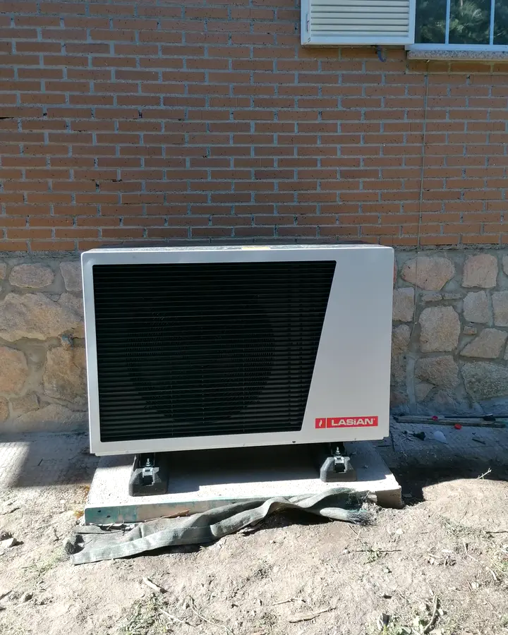 Unidad exterior de aerotermia Lasian sobre una losa junto al zócalo de piedra de una casa de ladrillo. Instalación de Guzmán Calefacción