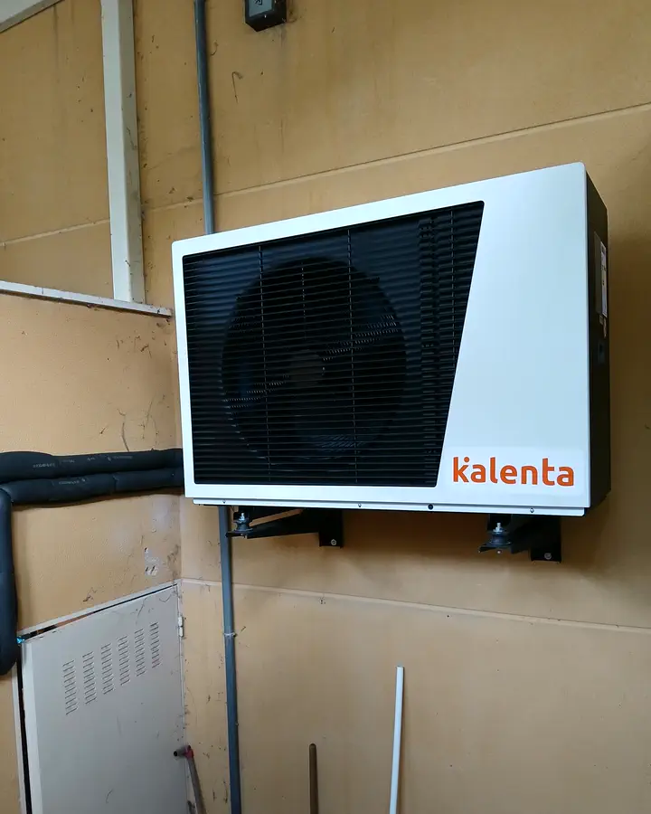 Unidad exterior de aerotermia Kalenta montada en pared con soportes en un patio. Instalación de Guzmán Calefacción