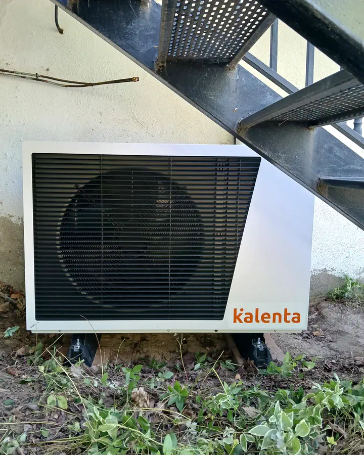 Instaladores de calefacción en Collado Mediano 6 Unidad exterior de aerotermia Kalenta instalada bajo una escalera metálica exterior. Instalación de Guzmán Calefacción