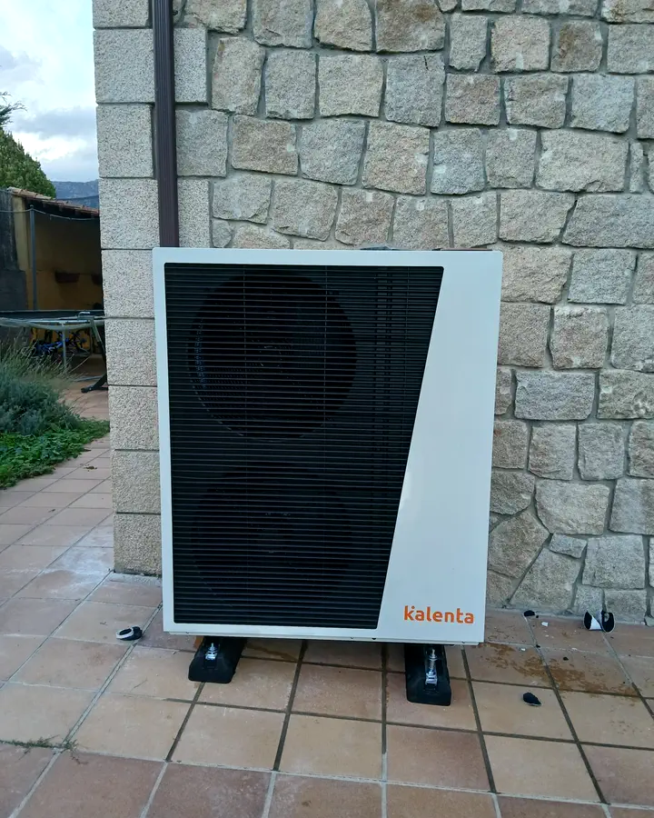 Unidad exterior de aerotermia Kalenta sobre una terraza de baldosa junto a un muro de piedra. Instalación de Guzmán Calefacción