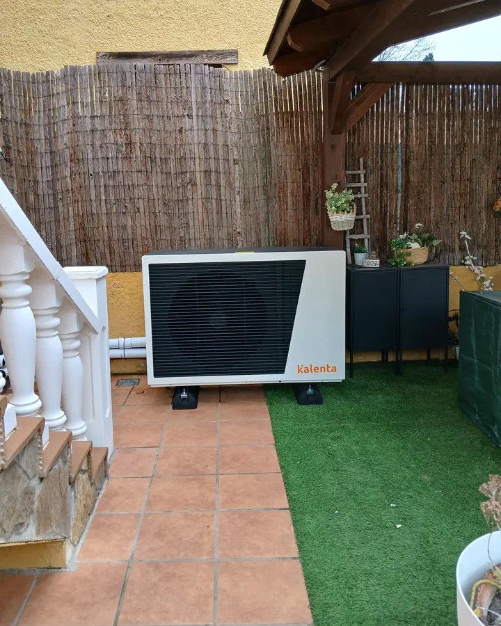 Unidad exterior de aerotermia Kalenta en un patio con césped artificial y cerramiento de cañizo. Instalación de Guzmán Calefacción