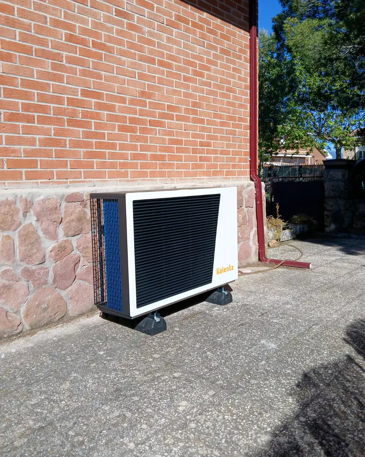 Unidad exterior de aerotermia Kalenta junto a un zócalo de piedra en el exterior de una vivienda. Instalación de Guzmán Calefacción